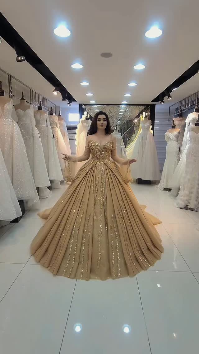 Gold and Champagne Wedding: 7 Ideas for a Warm, Metallic Celebration 5 Woman wearing a voluminous sparkling gold ball gown in a bridal boutique surrounded by white wedding dresses.