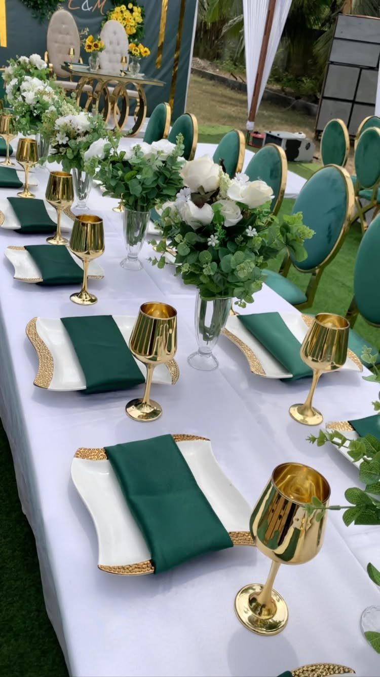 Green Wedding Colors: 8 Palettes From Olive to Emerald 4 A wedding table set with emerald green napkins, gold goblets, and white floral centerpieces on a white cloth.