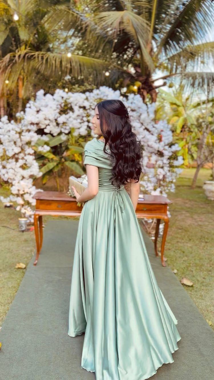 Green Wedding Colors: 8 Palettes From Olive to Emerald 5 Woman in a long sage green satin gown standing outdoors near white flowers and palm trees.
