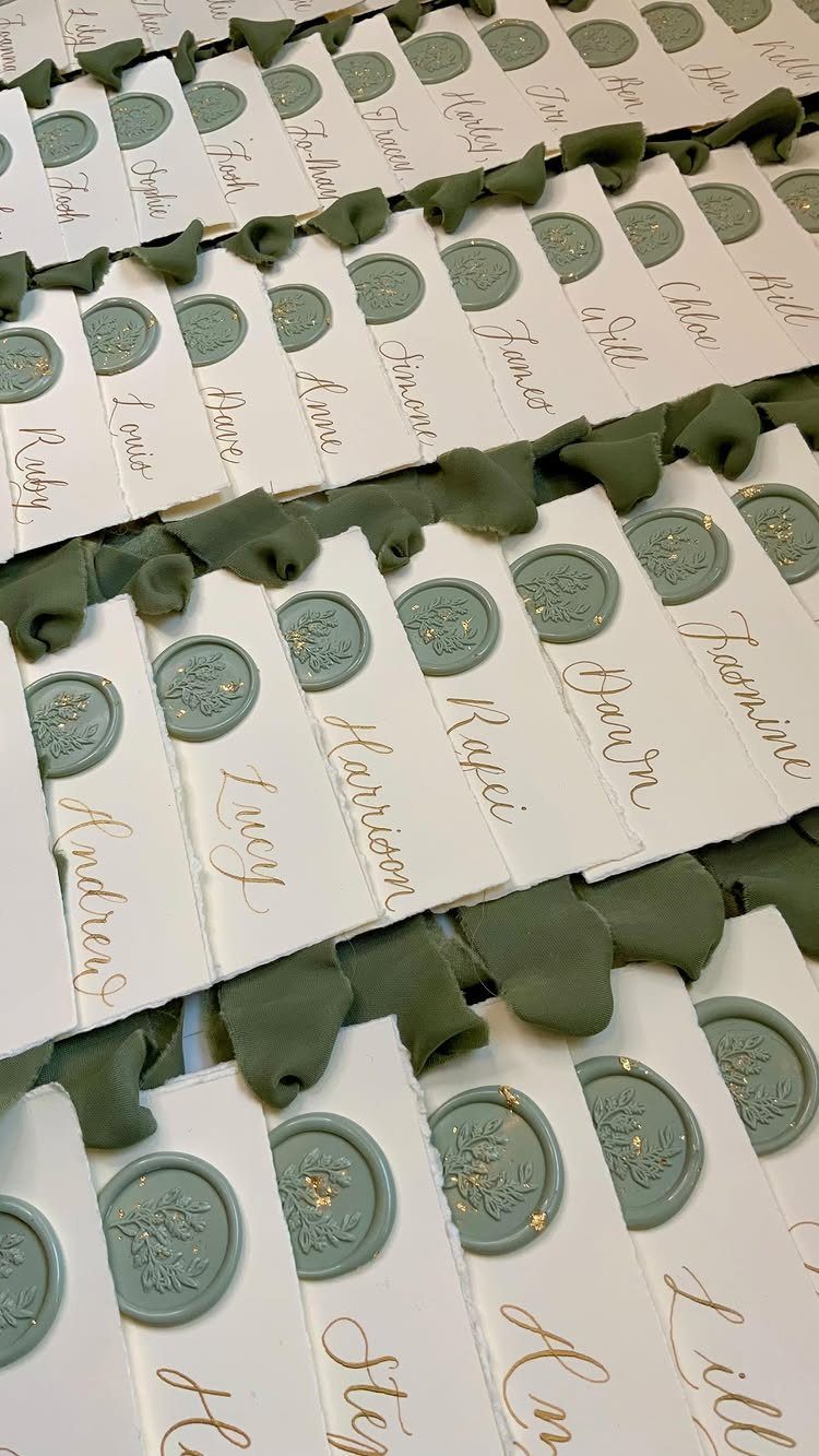Green Wedding Colors: 8 Palettes From Olive to Emerald 3 White place cards with sage green wax seals and gold calligraphy arranged in rows.