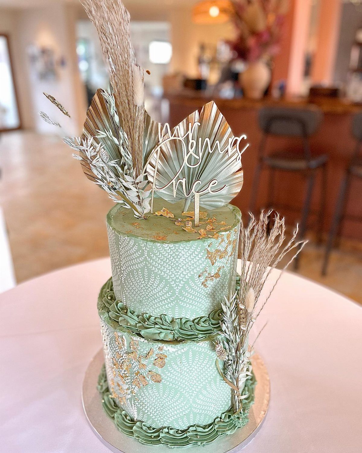 Green Wedding Colors: 8 Palettes From Olive to Emerald 7 A two-tiered sage green wedding cake decorated with gold leaf and dried botanical elements.