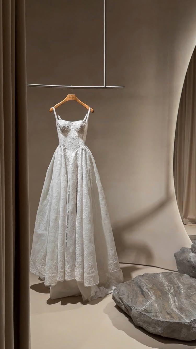 White lace A-line wedding dress hanging on a wooden hanger in a minimalist studio setting.