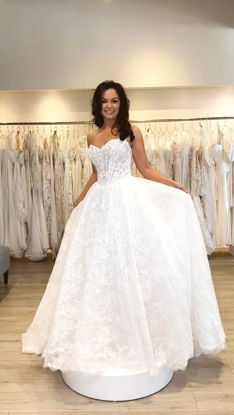 Woman posing in a white lace wedding dress with a sweetheart neckline and full skirt.