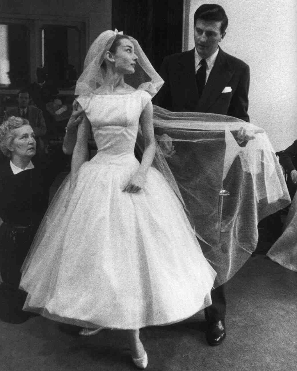 A woman in a white tea-length wedding dress and veil standing with a man in a suit.