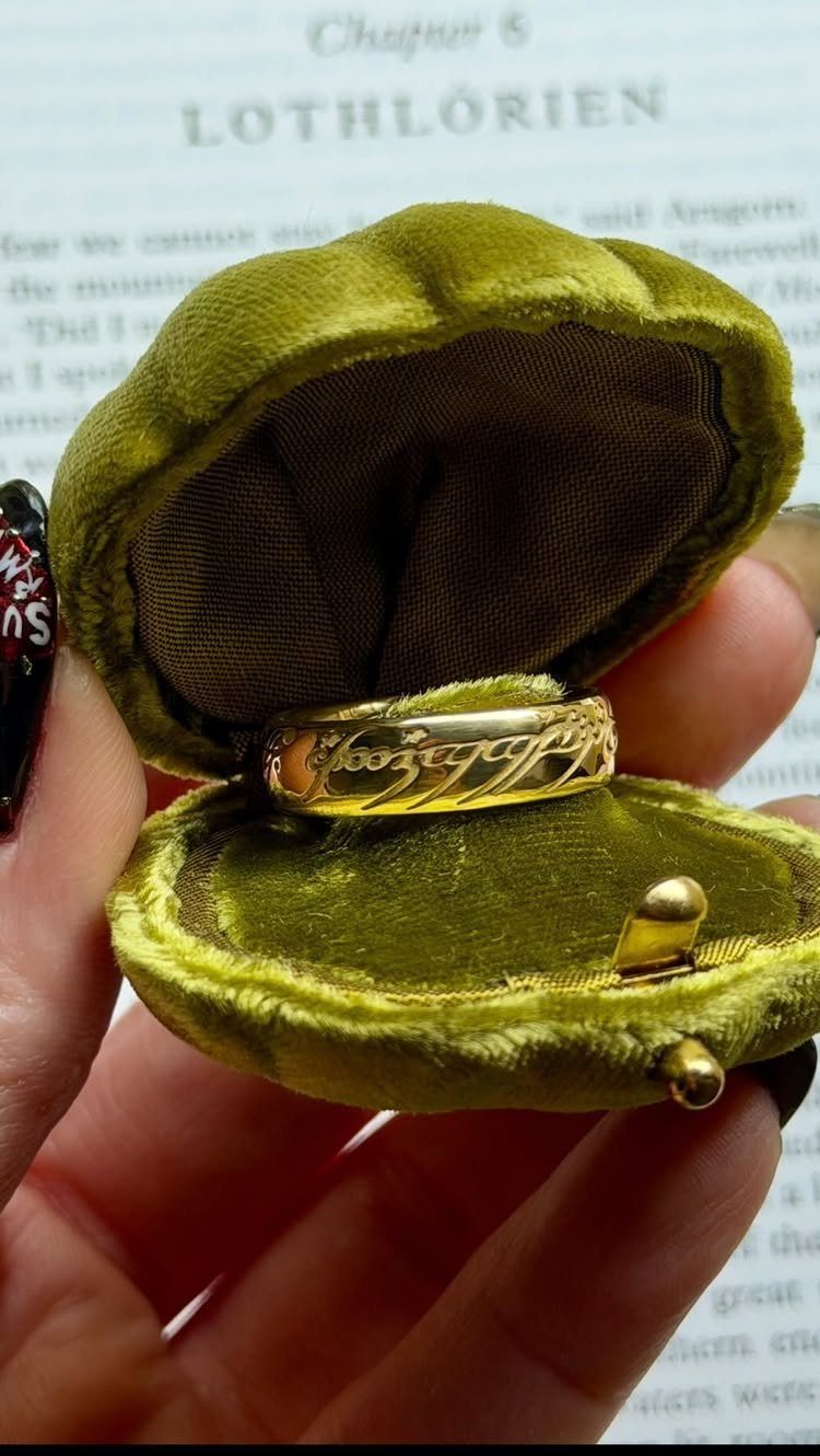 A gold ring with elvish inscriptions inside a green velvet ring box.