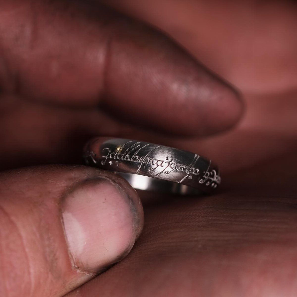 A silver ring featuring elven-style script engravings held between two fingers.