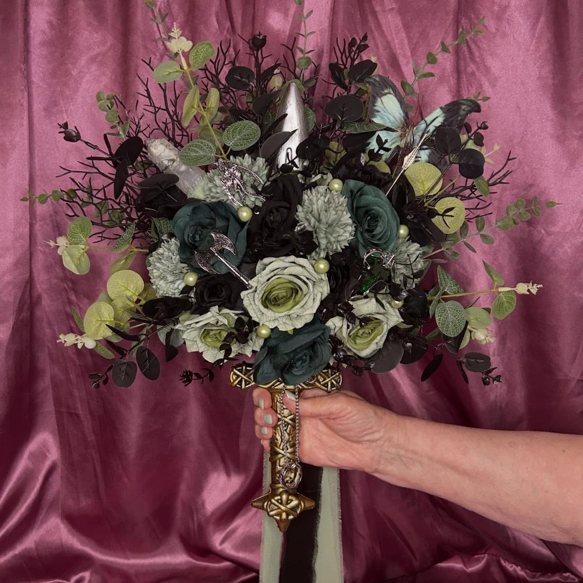 A hand holding a dark green and cream rose bouquet with butterfly accents.