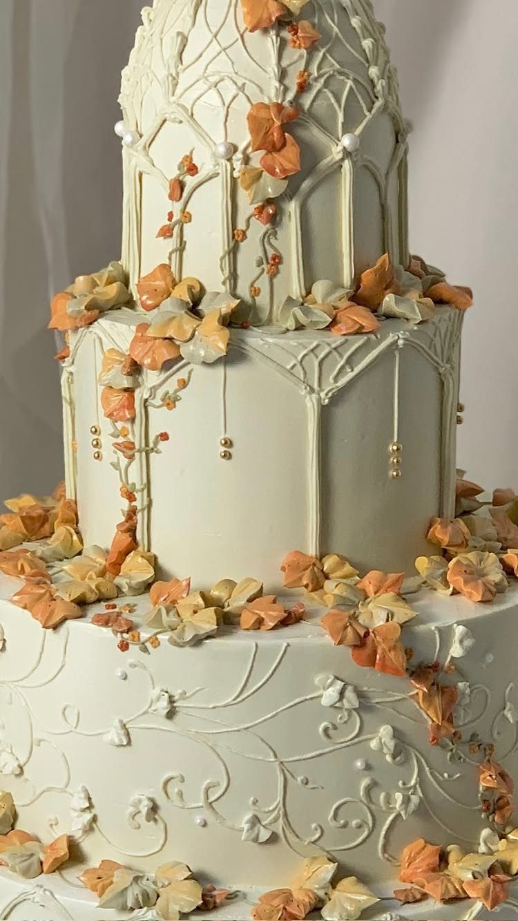 A multi-tiered white wedding cake decorated with cream frosting vines and orange autumn leaves.