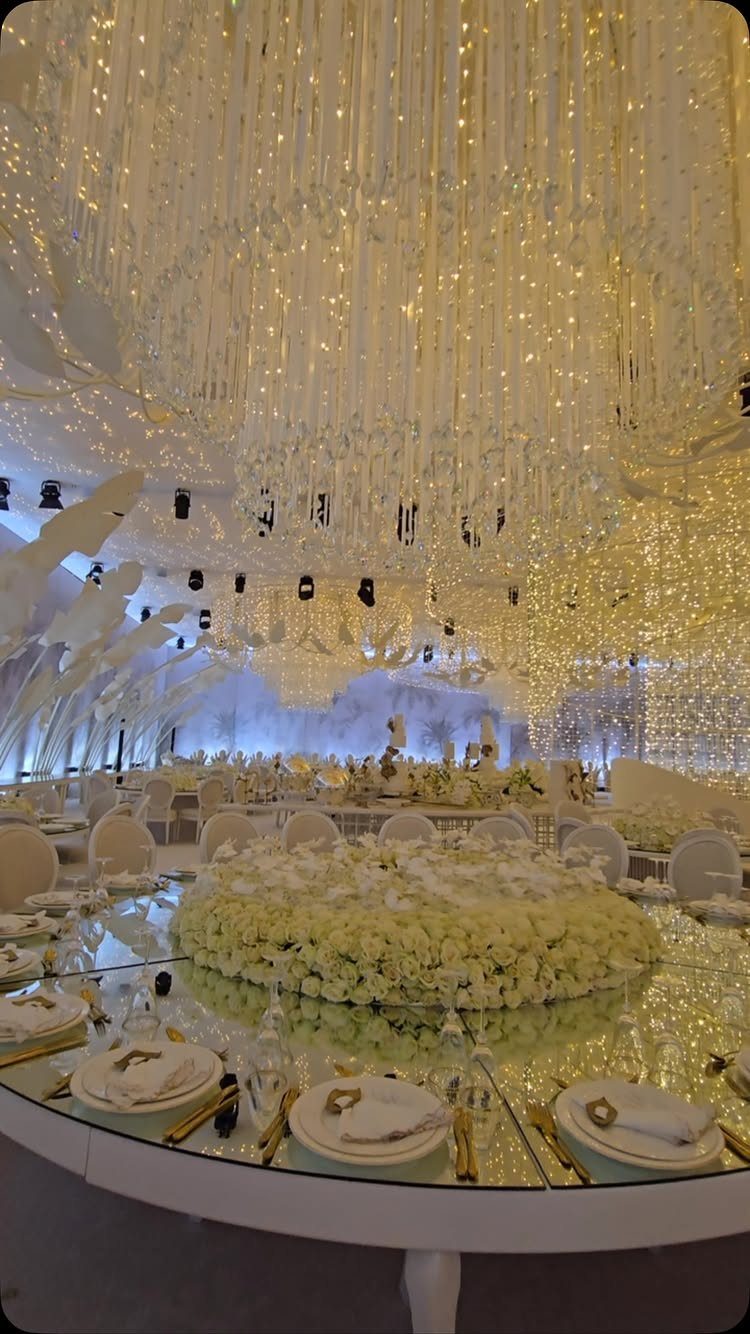 Cascading fairy light chandelier hanging above a luxury wedding banquet table with white flowers.