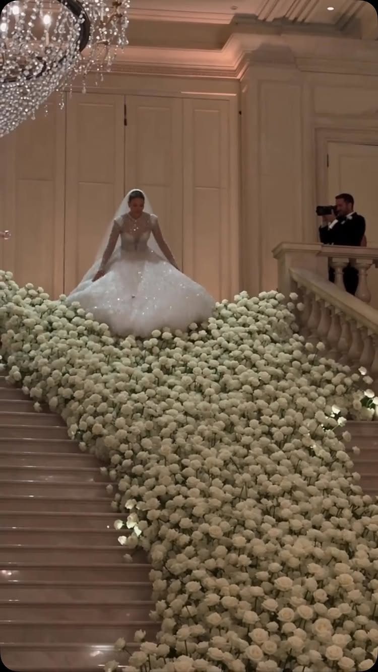 Bride in a white wedding dress walking down a staircase covered in white flowers.