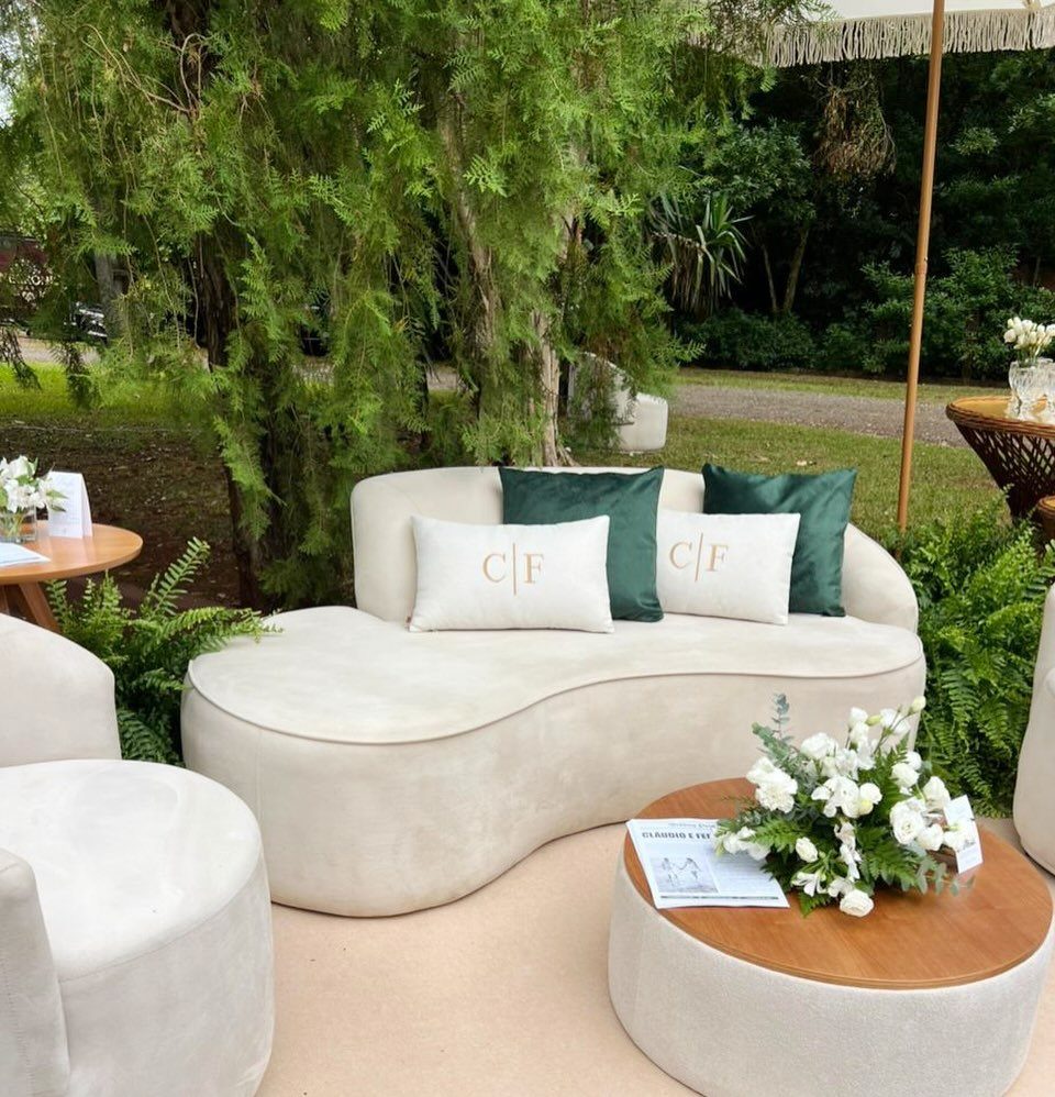 Cream velvet curved sofa with green and white pillows in a lush outdoor lounge setting.