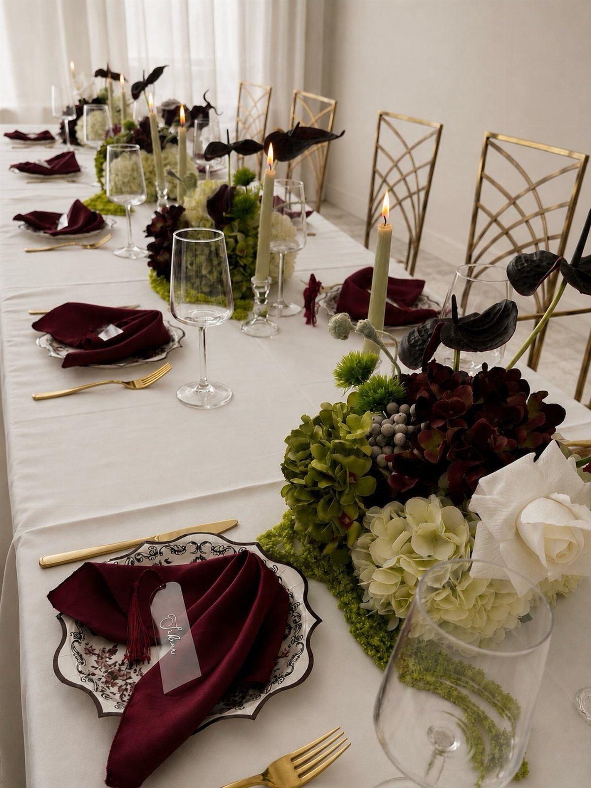 Wedding table setting with burgundy napkins, gold cutlery, and large hydrangea floral centerpieces.