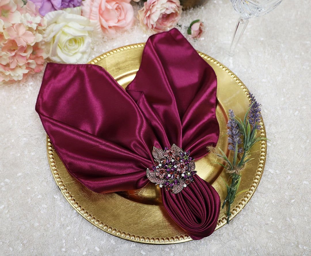Burgundy satin napkin with a jeweled ring on a gold charger plate.