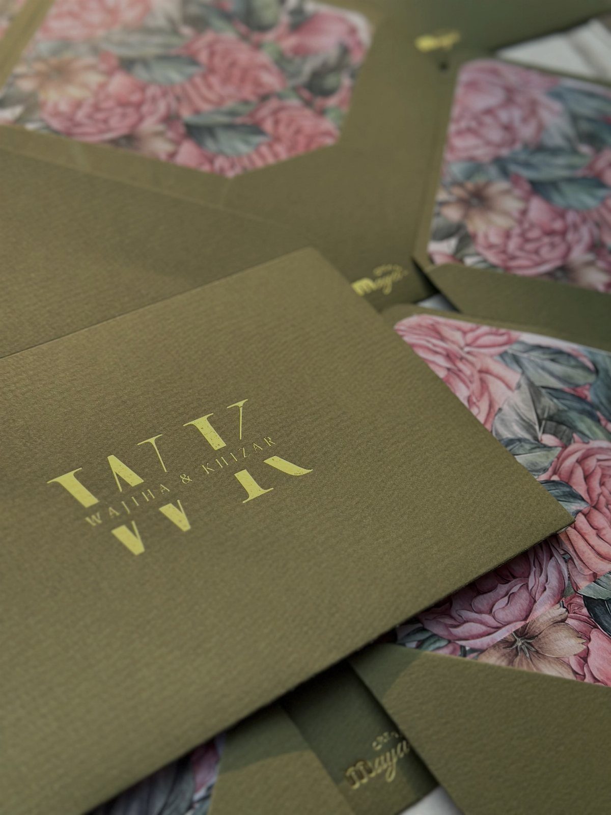 Olive green wedding invitations with gold foil text and floral patterned envelopes.