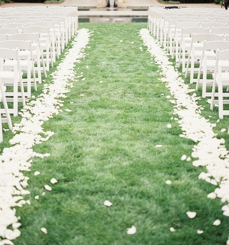 10 Outdoor Wedding Aisle Decor Ideas with Photos 10 White flower petals lining the edges of a green grass wedding aisle between rows of white chairs.