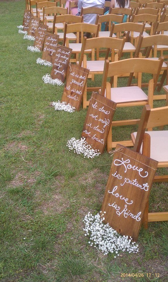 10 Outdoor Wedding Aisle Decor Ideas with Photos 5 Wooden signs with white quotes leaning against chairs on a grassy lawn with white flowers.