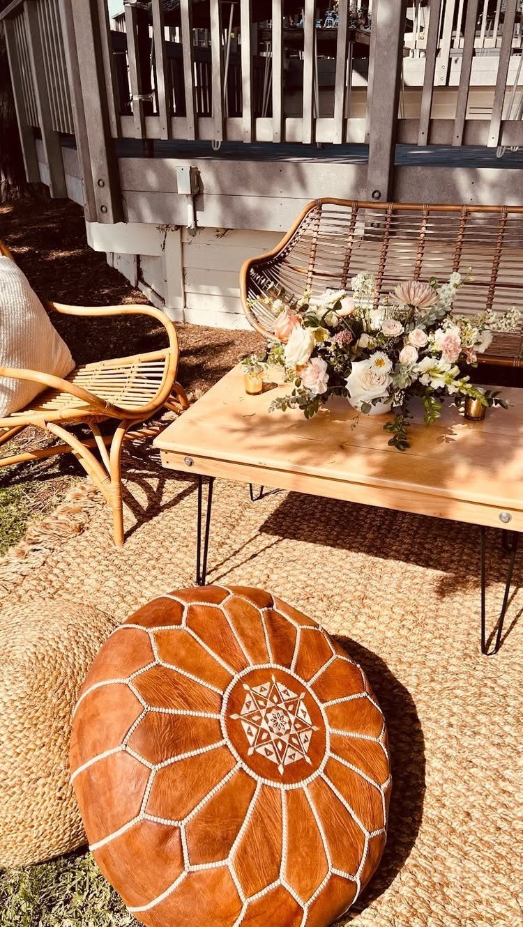 A wooden coffee table with flowers, a rattan chair, and a leather pouf on a rug.