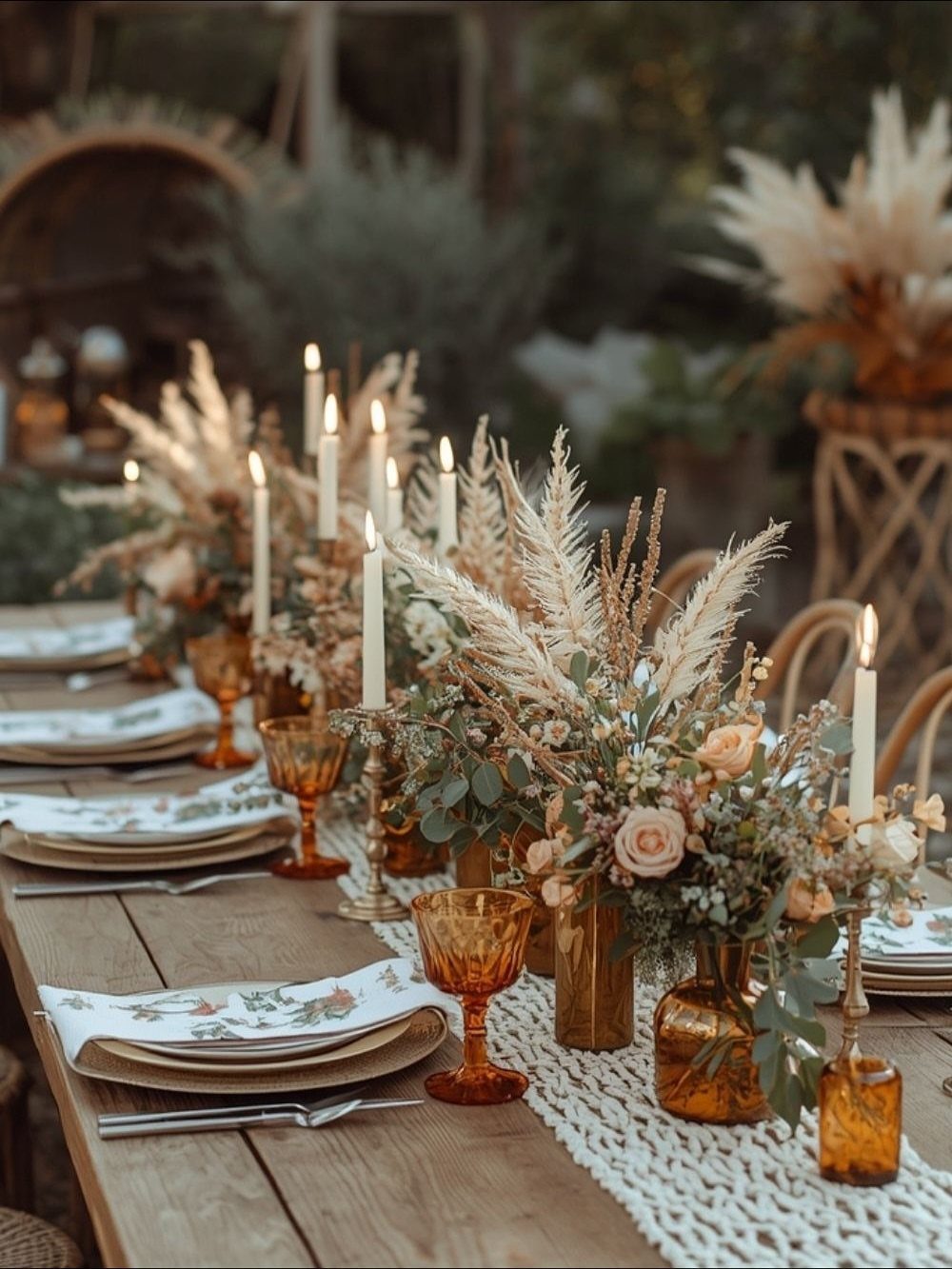 A rustic wooden table set with floral arrangements, amber glasses, and white taper candles.