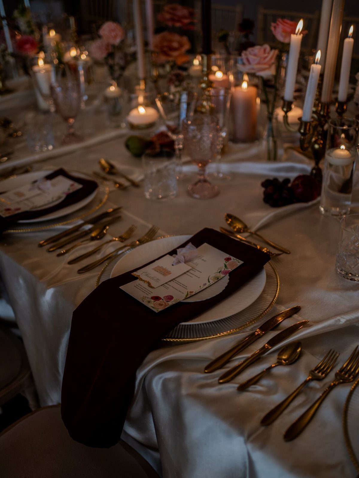 12 Ideas for a Red and White Wedding Theme 2 Elegant wedding table setting with gold cutlery, white plates, and burgundy napkins under warm candlelight.