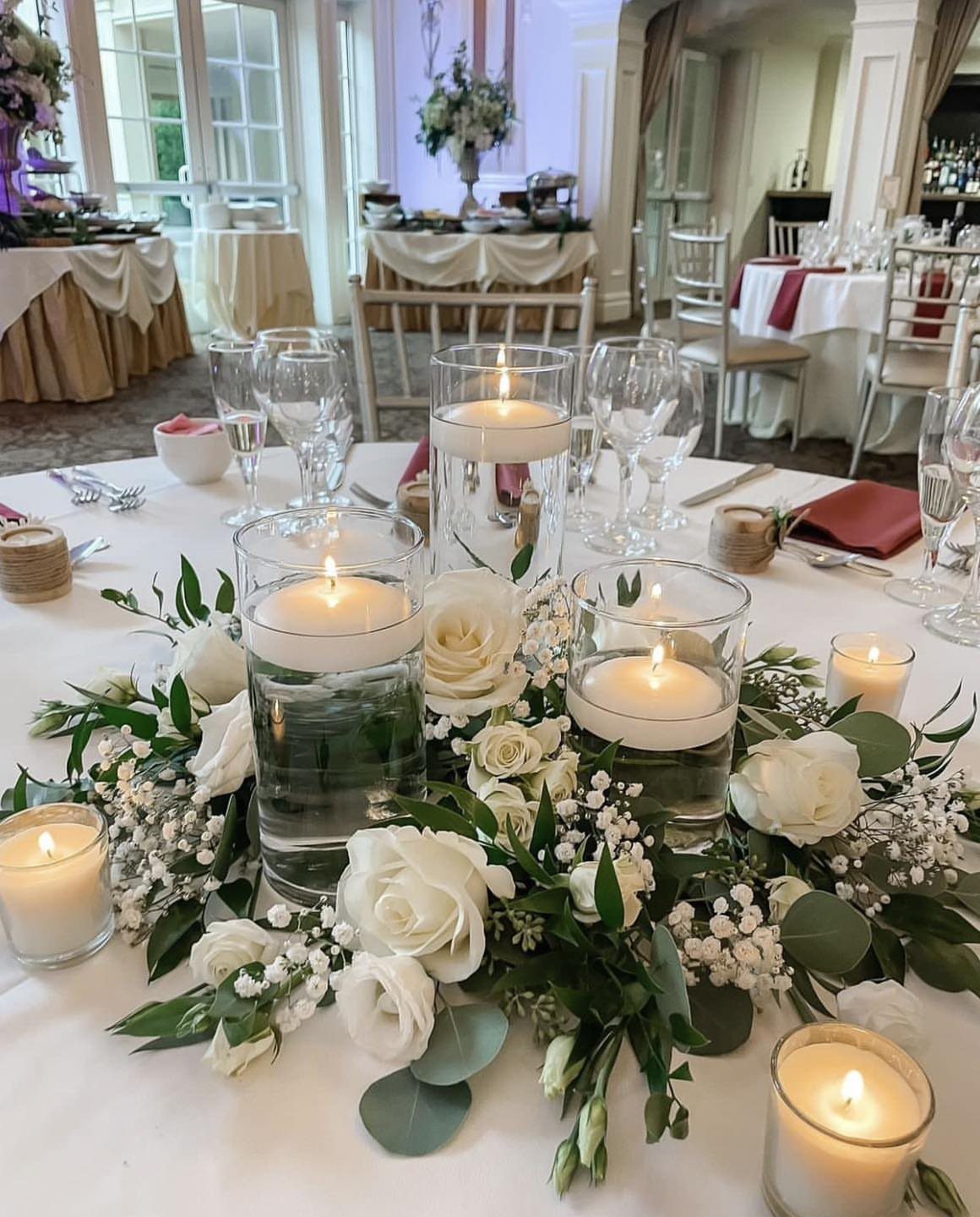 12 Ideas for a Red and White Wedding Theme 7 White floating candles in glass cylinders nestled within a white rose and greenery centerpiece on a table.