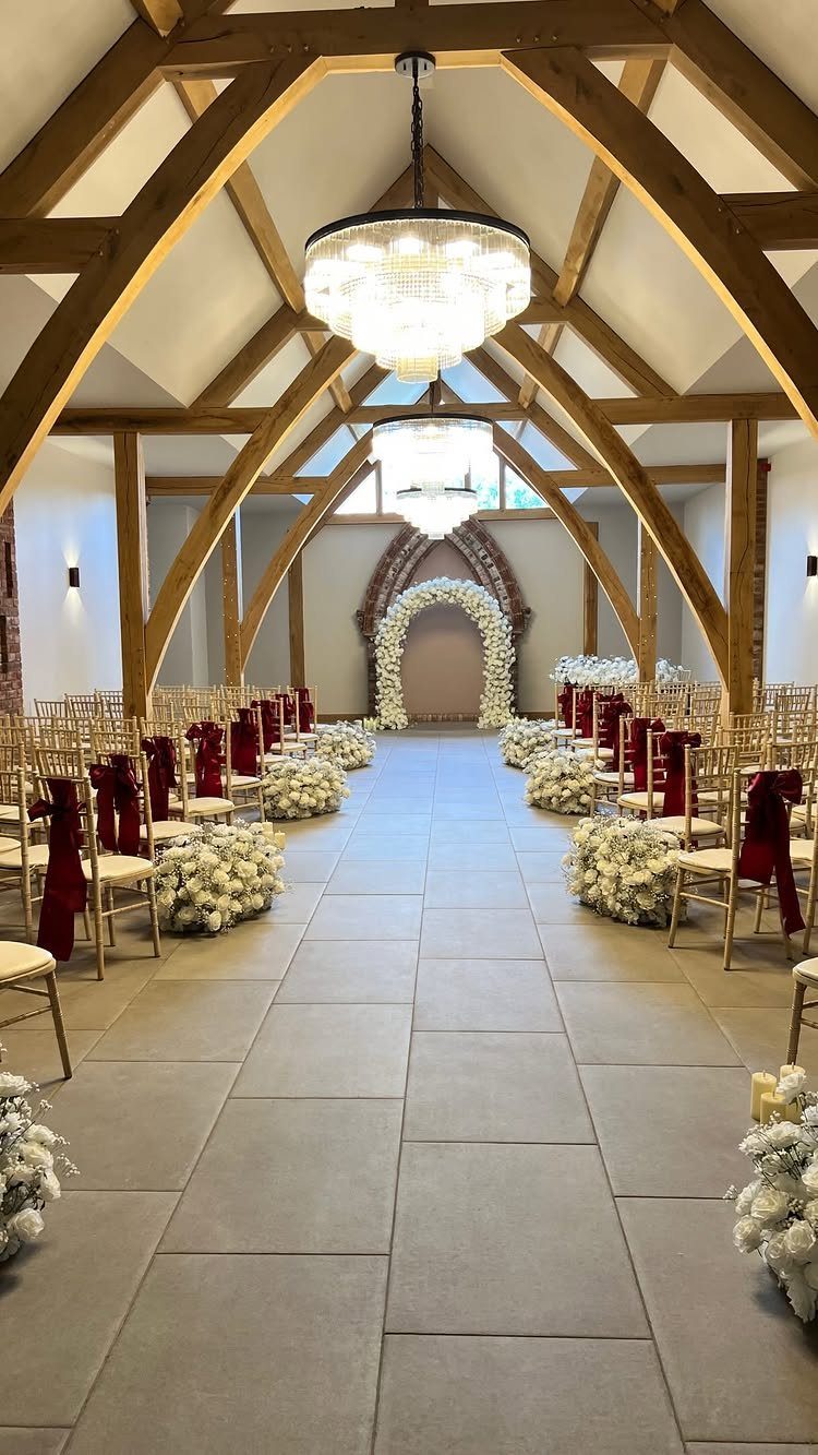 12 Ideas for a Red and White Wedding Theme 9 Gold chiavari chairs with burgundy satin sashes line a wedding ceremony aisle with white flowers.