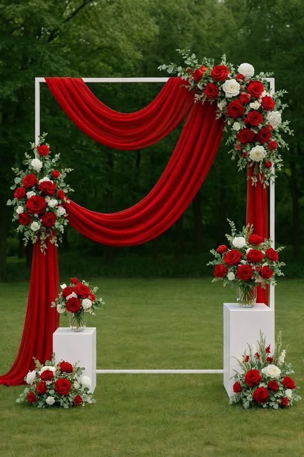 12 Ideas for a Red and White Wedding Theme 11 A white wedding arch with red fabric drapes and red and white floral arrangements on grass.