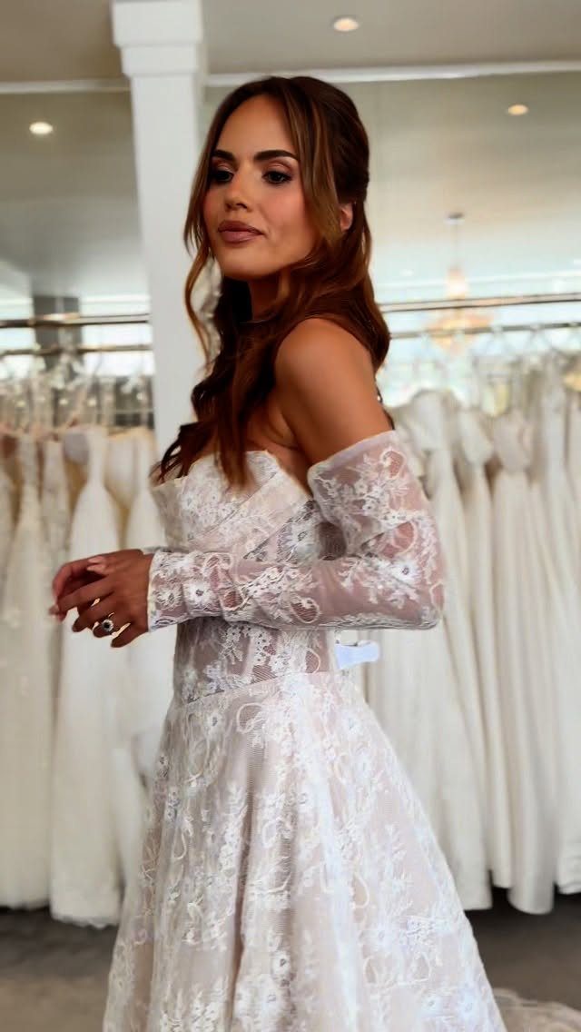 Woman wearing a strapless lace wedding dress with long detachable lace sleeves in a boutique.