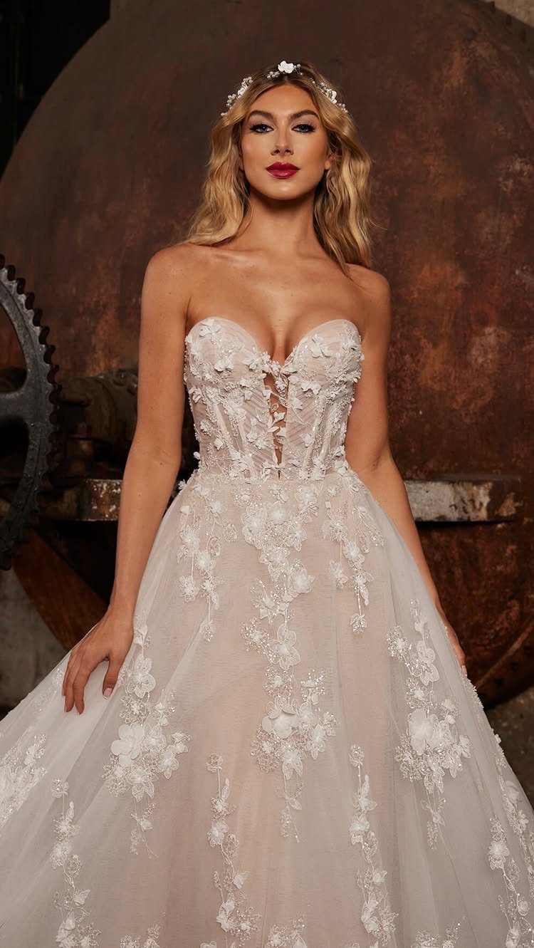 Woman posing in a strapless A-line wedding dress with floral lace detailing and a tulle skirt.