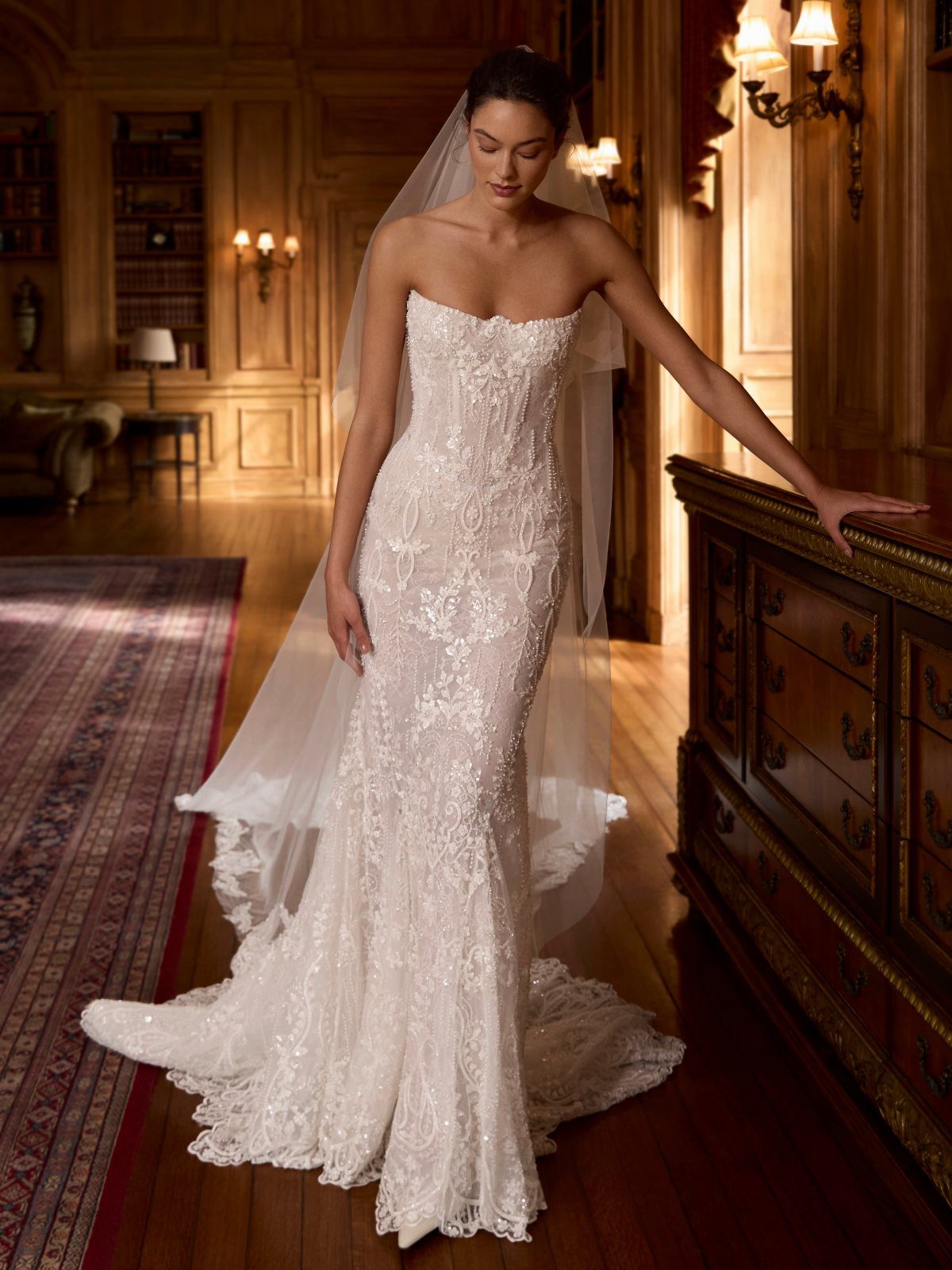 A woman in a strapless lace mermaid wedding dress standing in a wood-paneled room.