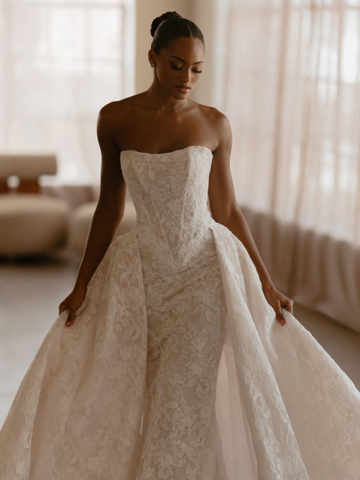 A woman posing in a strapless white lace wedding dress with a large tulle overskirt.