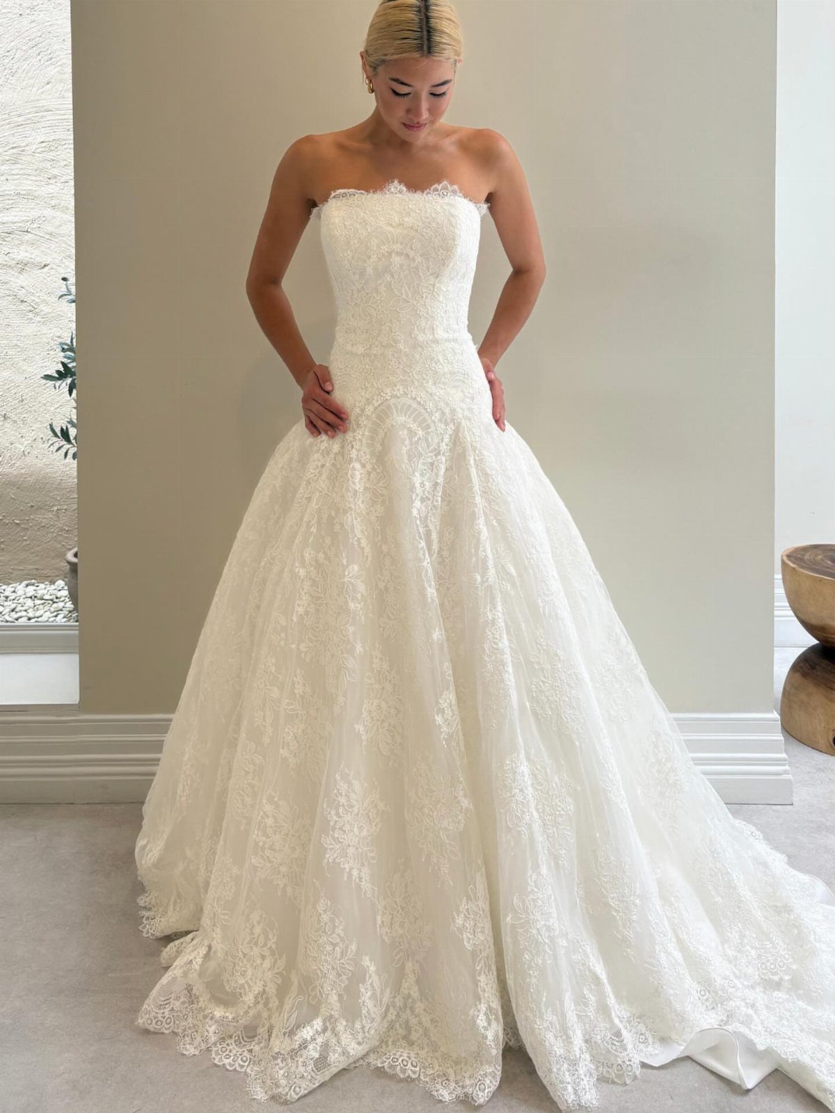 A woman posing in a white strapless lace wedding dress with a full skirt.