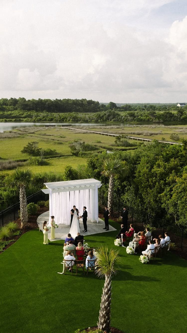 Wedding ceremony taking place on a green lawn under a white pergola with guests seated.
