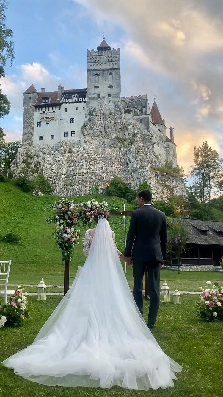 Bride and groom walking toward a floral arch with a large castle in the background.