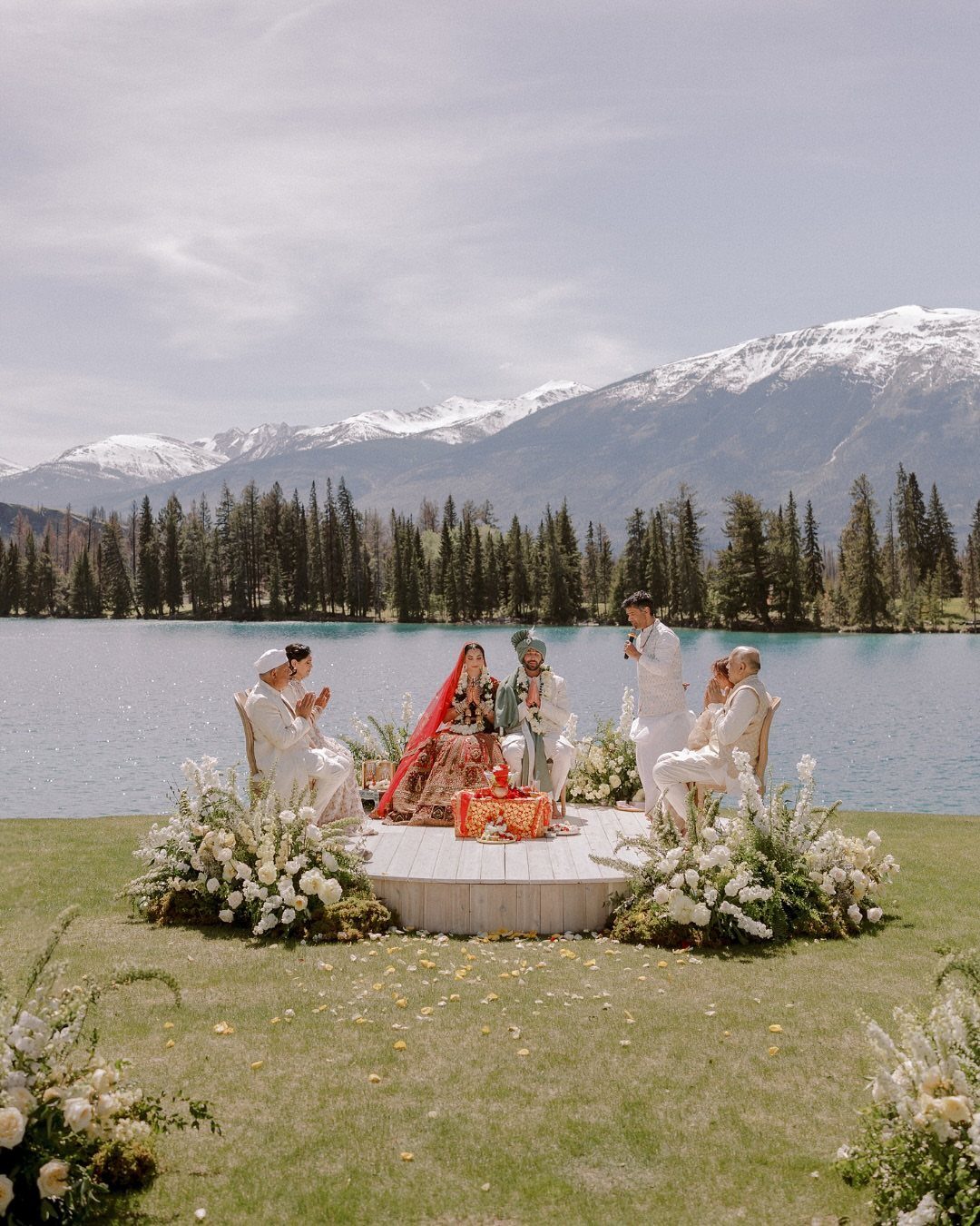 A wedding ceremony set on a wooden platform overlooking a lake and mountains.