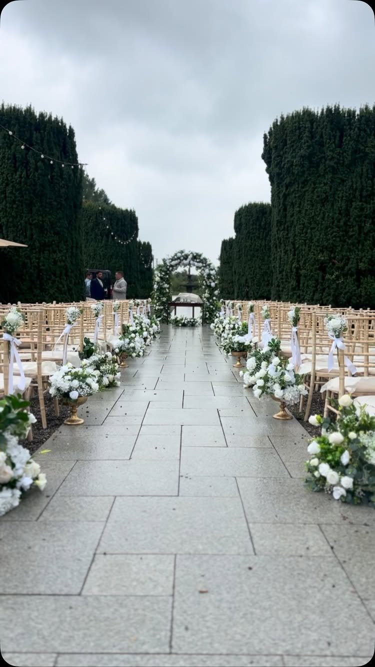 Wedding ceremony aisle with gold chairs and white floral arrangements leading to an archway.