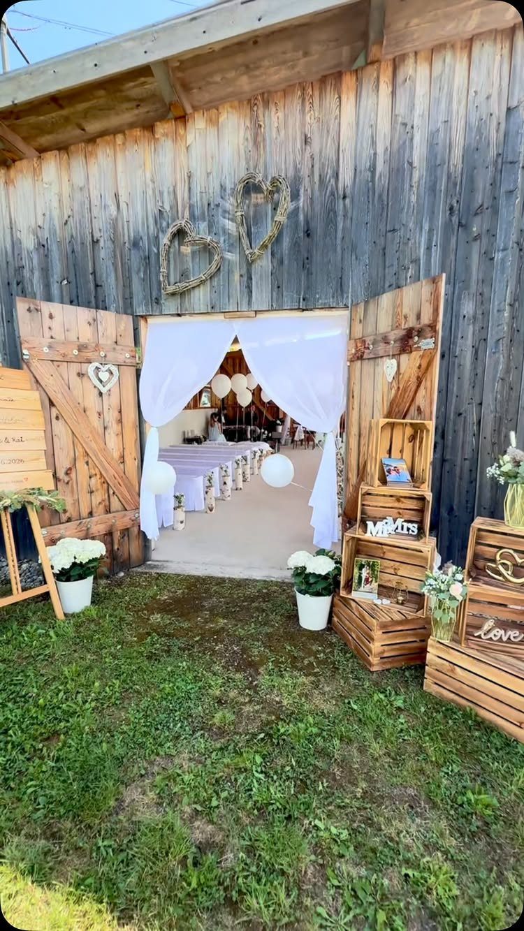 Rustic barn entrance decorated with white fabric, heart wreaths, and wooden crates for a wedding ceremony.