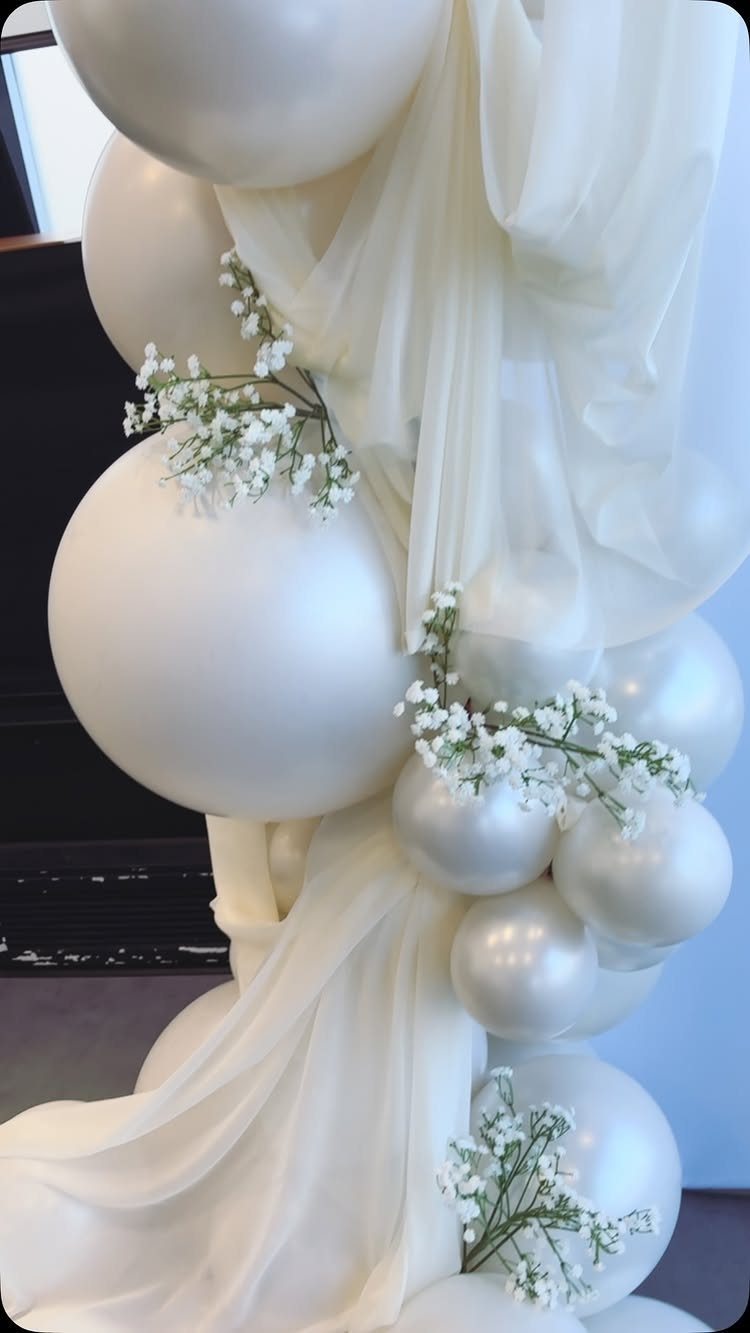 Cream and white balloons decorated with baby's breath and draped in flowing white tulle fabric.