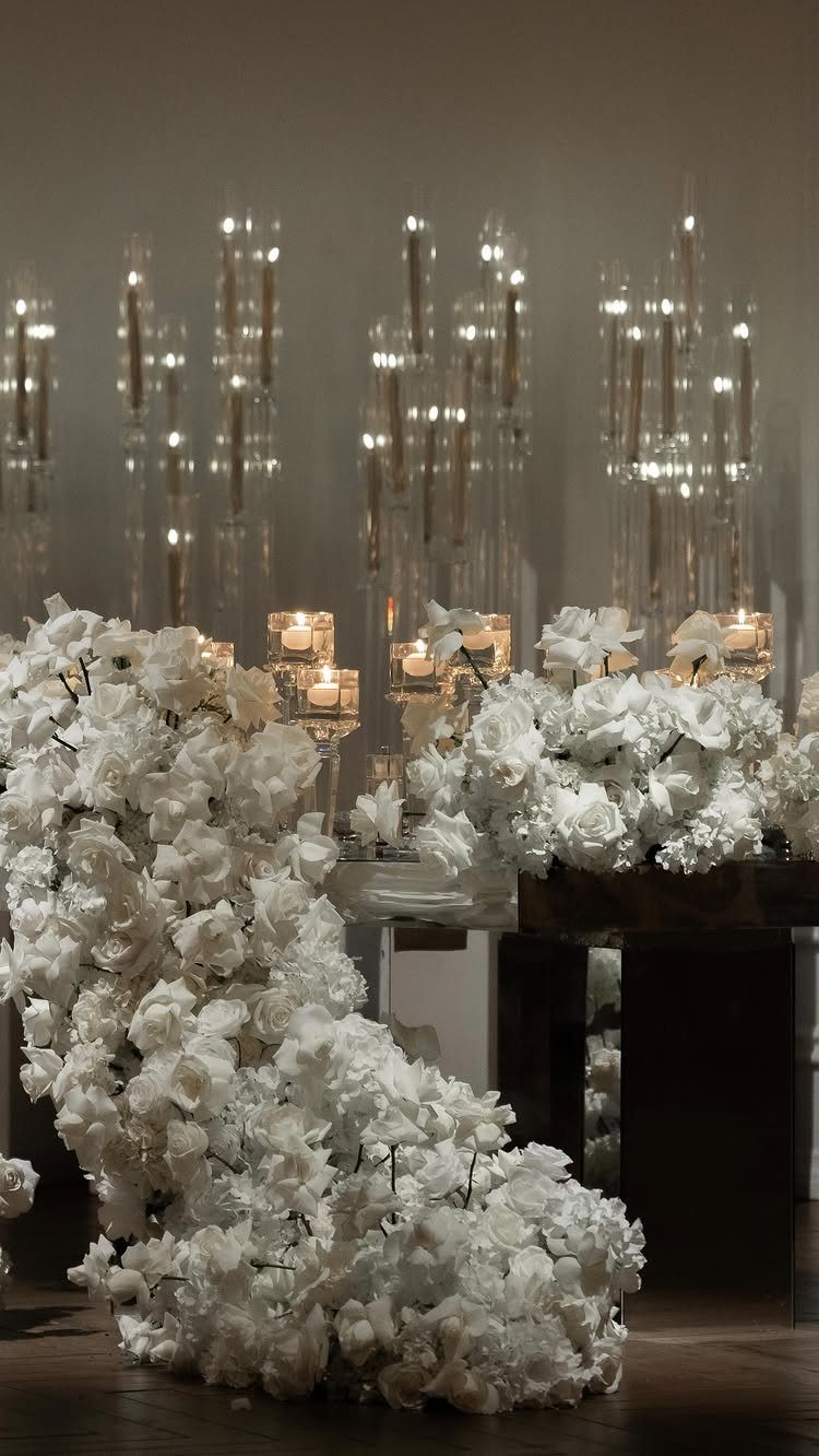 White flowers cascade beside tall glass candle holders with glowing tea lights in a dimly lit setting.