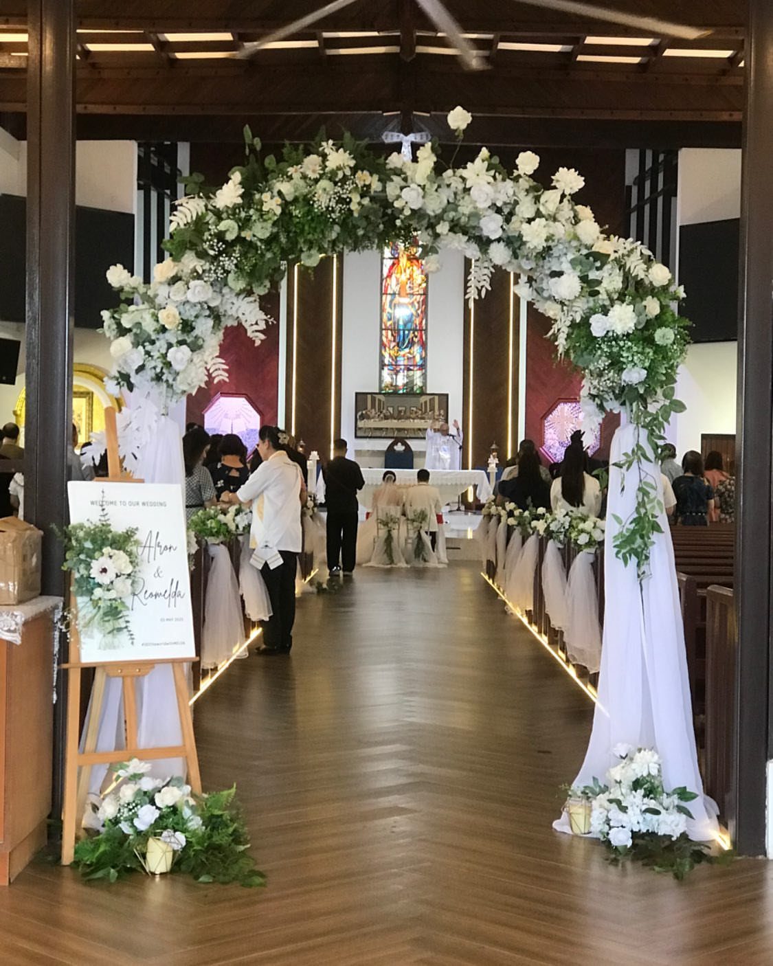 A white floral arch with greenery stands at the entrance of a church aisle.
