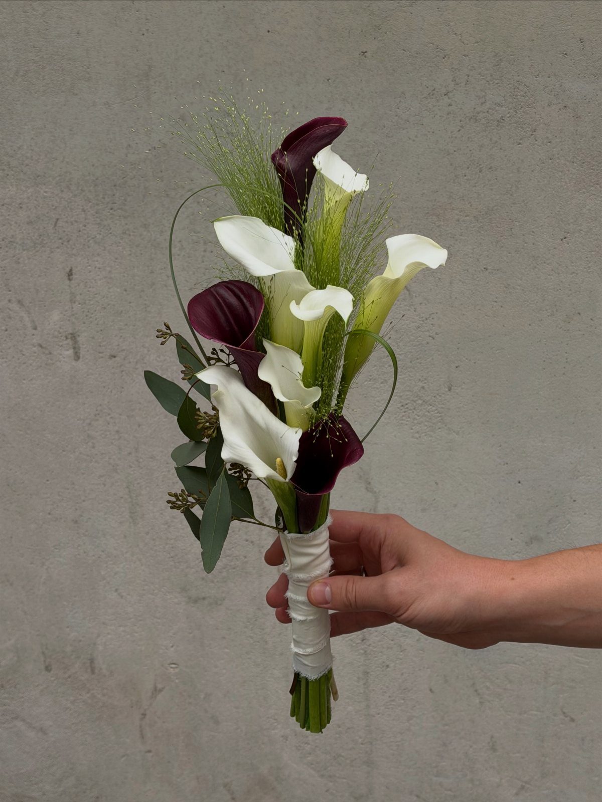 Wedding Decorations and Flowers: 8 Ideas for Ceremony to Reception 2 A hand holding a small bouquet of white and burgundy calla lilies wrapped in white ribbon.