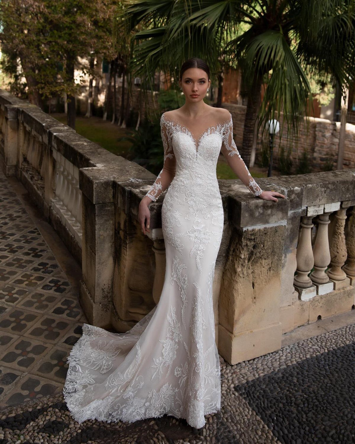Wedding Dress Long Sleeve: 7 Styles From A-Line to Turtleneck 3 Woman wearing a white lace mermaid wedding dress with long sleeves standing by a stone wall.