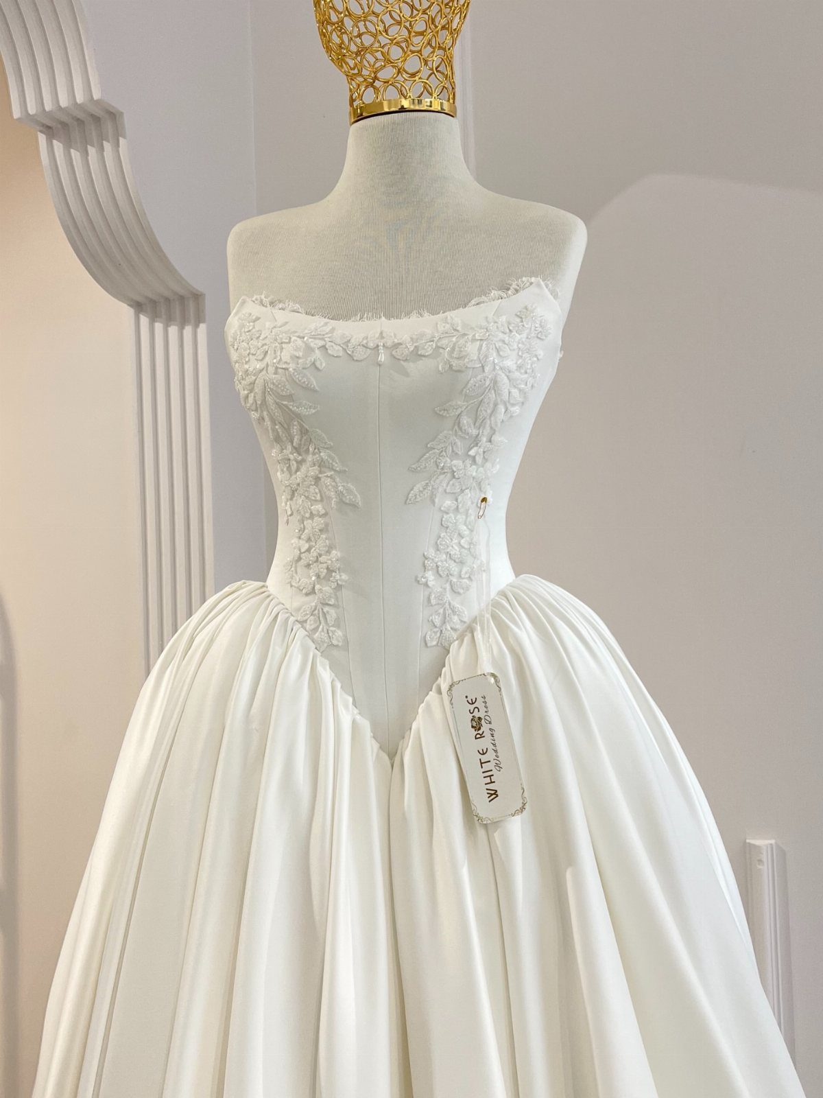 White strapless wedding dress with lace embroidery and a corset bodice on a mannequin.