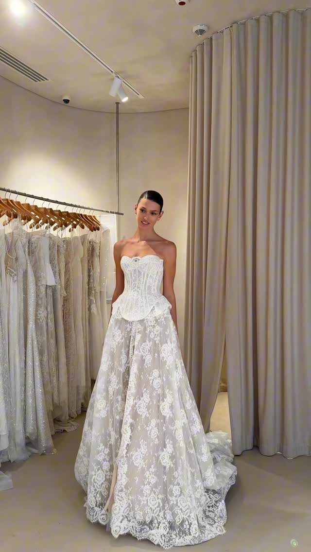 Woman posing in a strapless white lace wedding dress with a structured corset bodice.