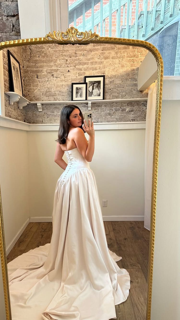 Woman in a white strapless wedding dress with a corset back taking a mirror selfie.