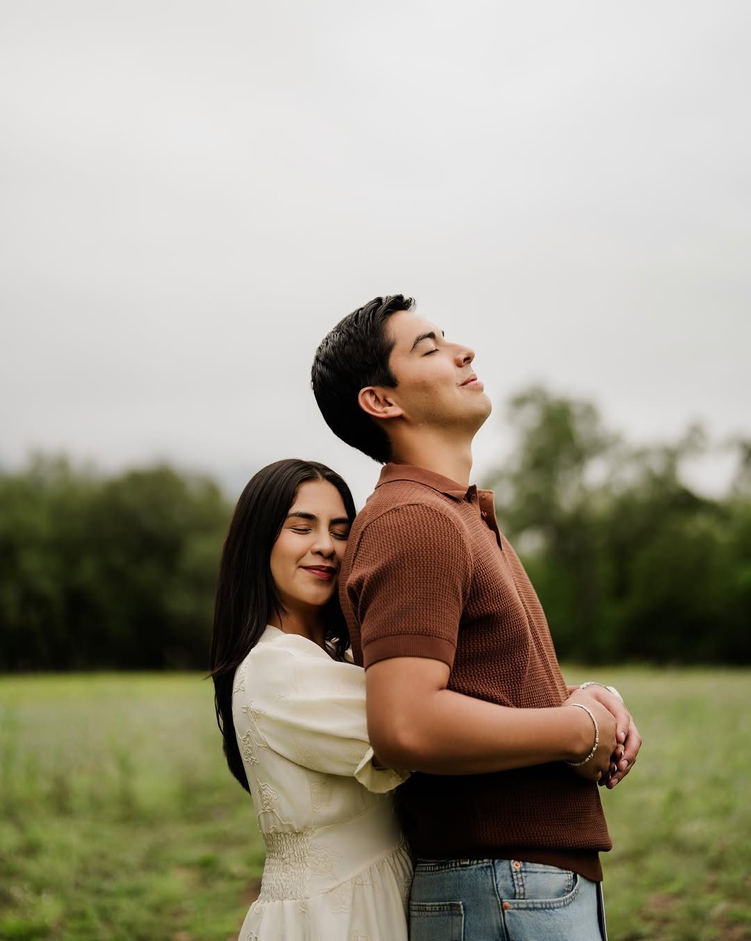 A man in a brown polo and a woman in white embracing in a field.