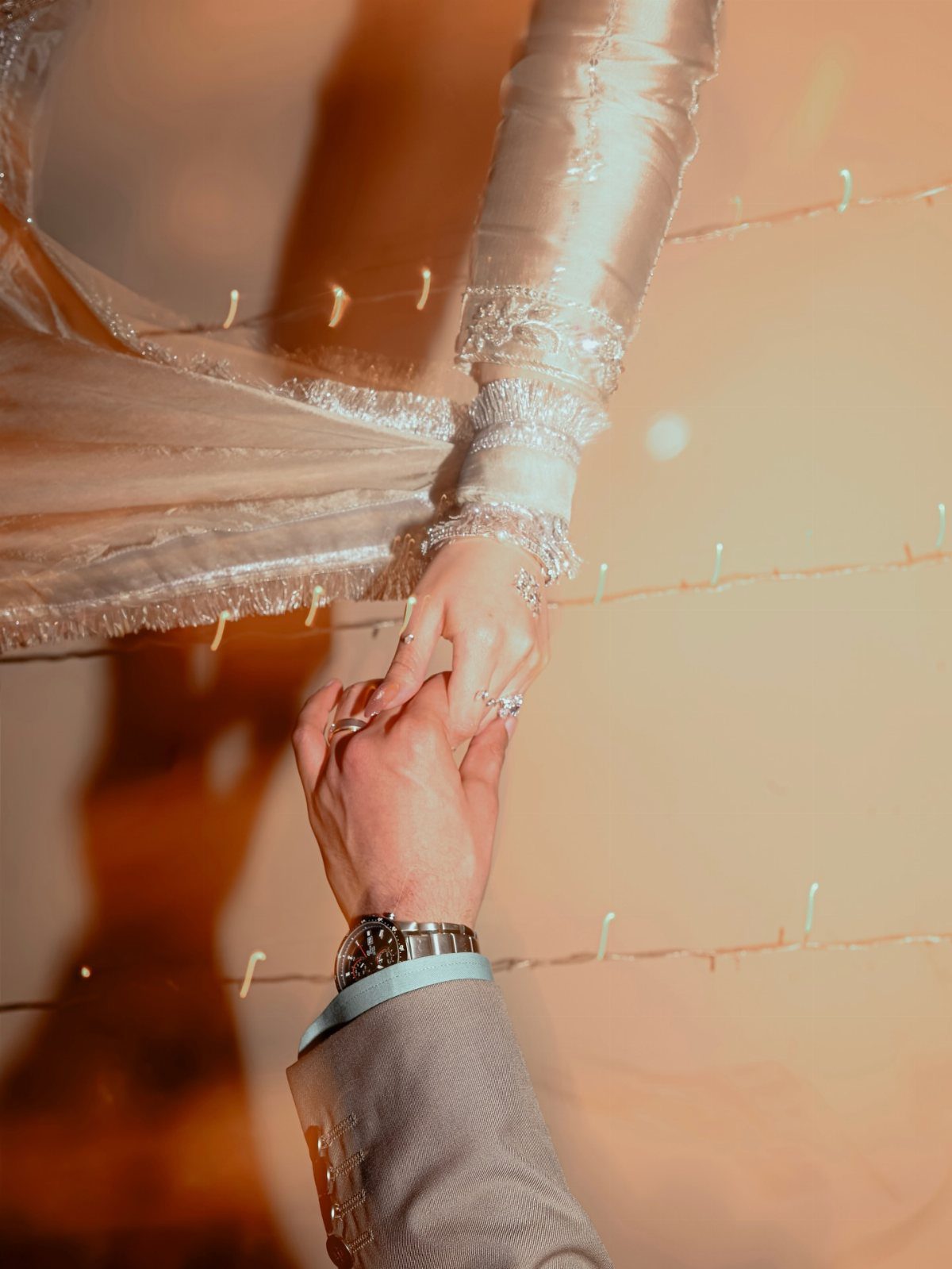 A close-up of a couple holding hands, showing a lace sleeve and a suit sleeve.