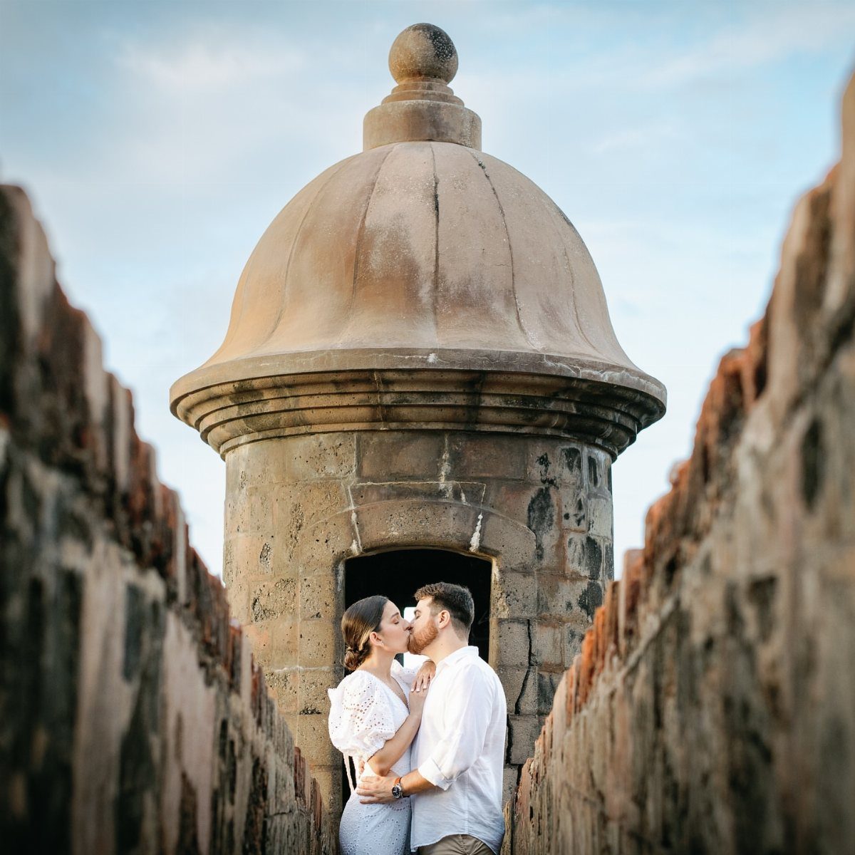 A couple kissing between stone walls beneath a large architectural dome.