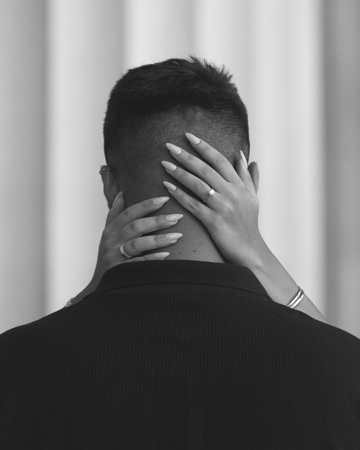 A woman's hands with rings resting on a man's head and neck in black and white.