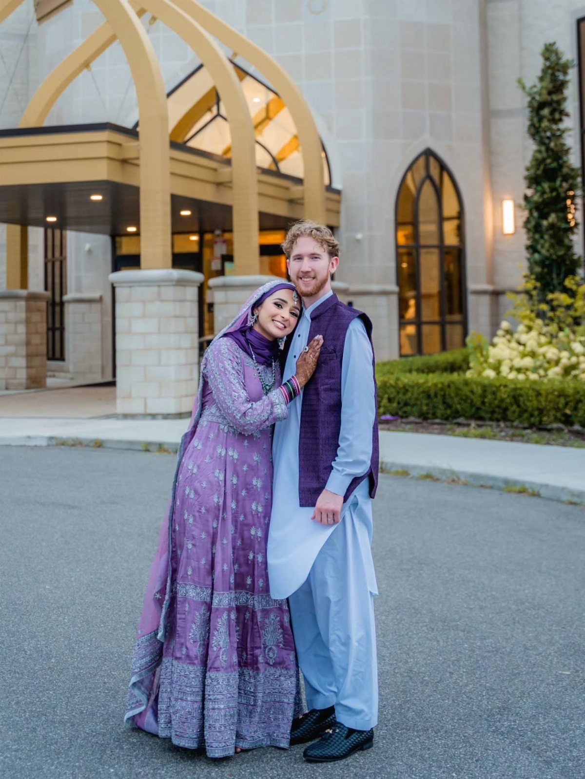 A couple in purple traditional South Asian clothing posing closely together outdoors.