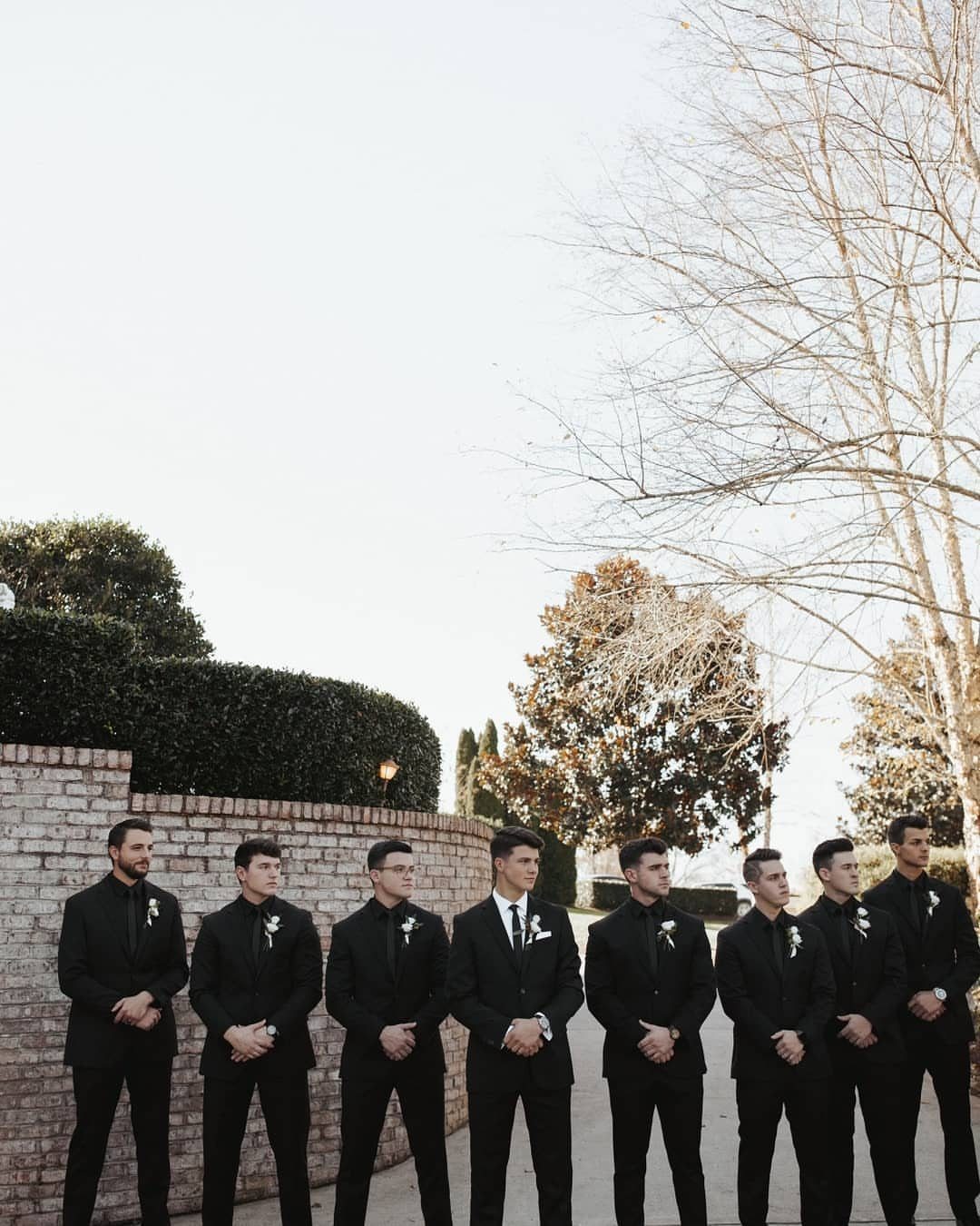 Eight men standing in a row wearing matching black suits and white boutonnieres.